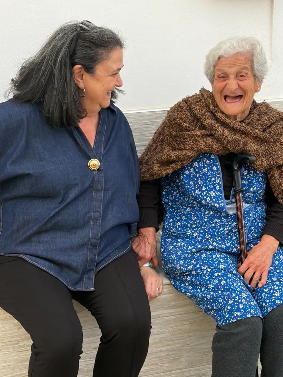 Two women laughing together on a bench in Basilicata